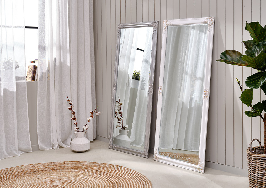 Speil og rundt teppe i et lyst rom med lange gardiner