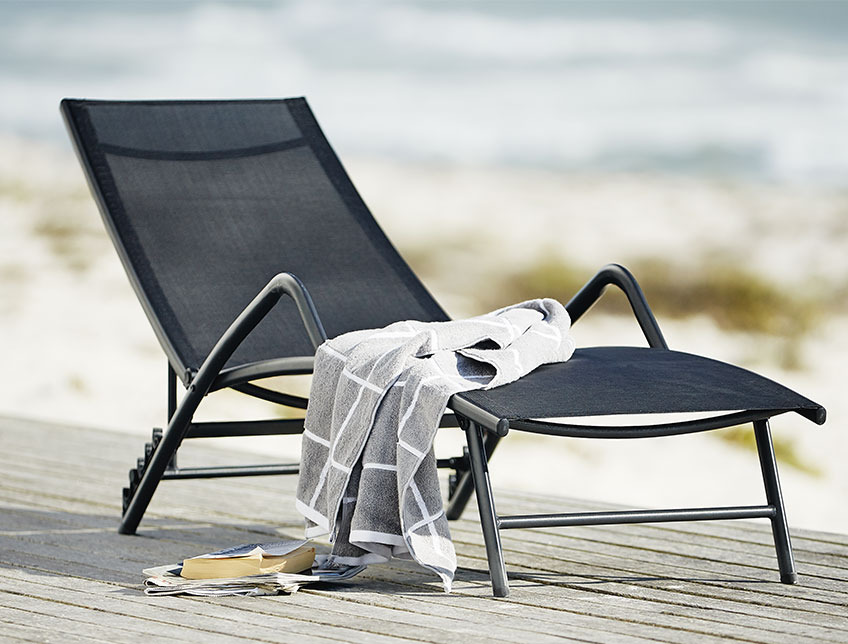 Sort solseng med armlener på en uteplass ved stranden