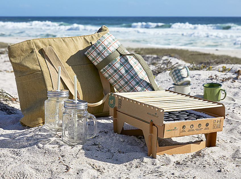Engangsgrill, kjølebag, piknikteppe, drikkeglass og kopper på stranden