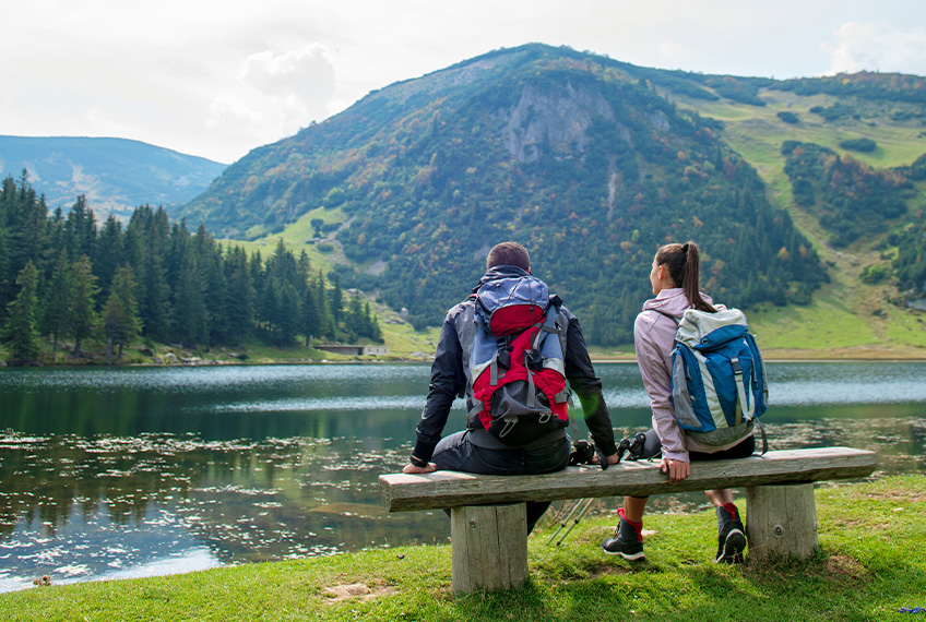 Mann og kvinne sitter på benk med utsikt over fjellet og innsjøen