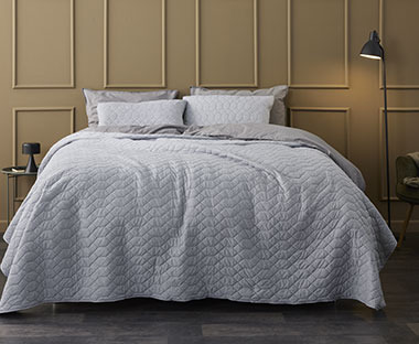 Grått sengeteppe med sømmer som skaper et elegant mønster