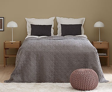 Grått sengeteppe med sømmer som danner et dekorativt mønster